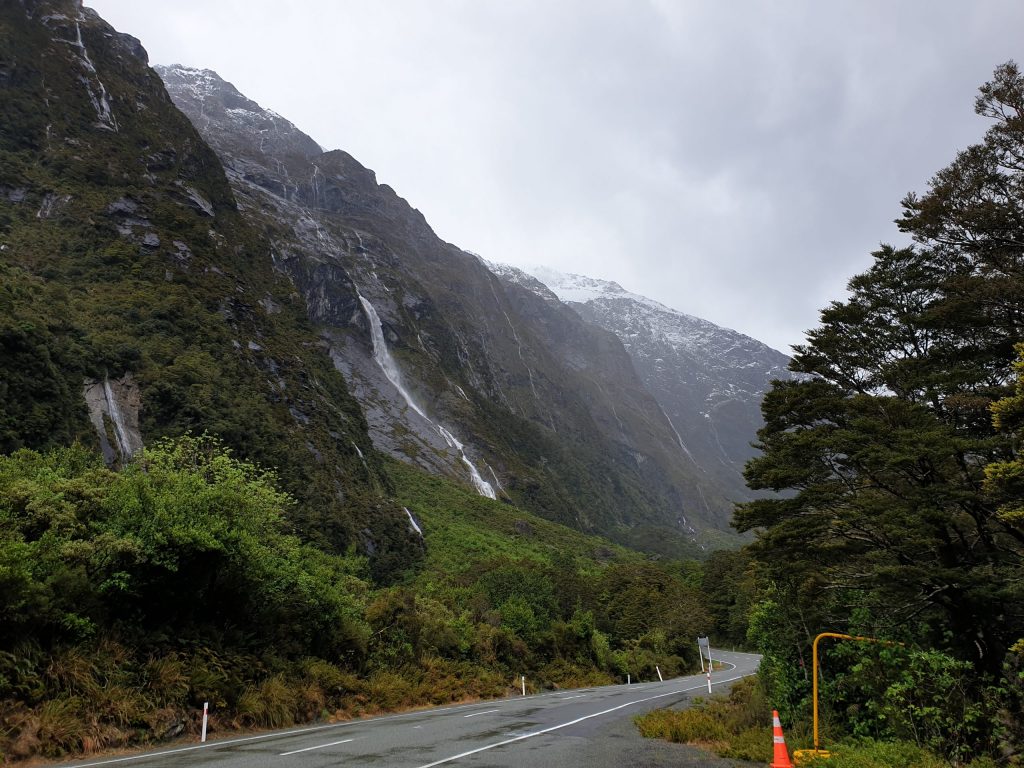 Image of road bordered by mountains with water running down towards the road in New Zealand