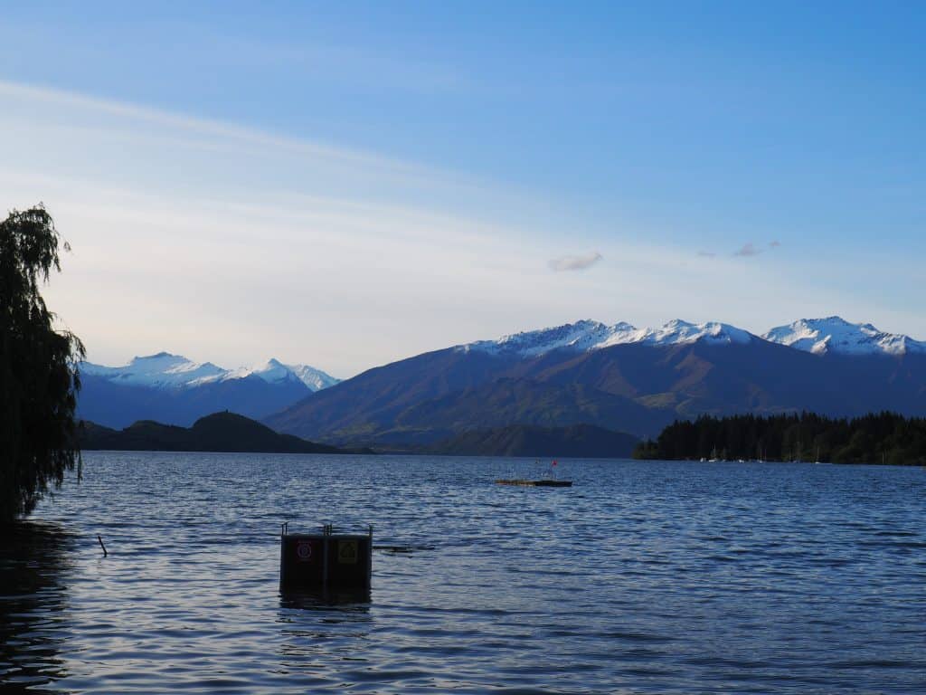 Garbage bins standing out in the water at Lake Wanaka, with the snow capped Southern Alps behind