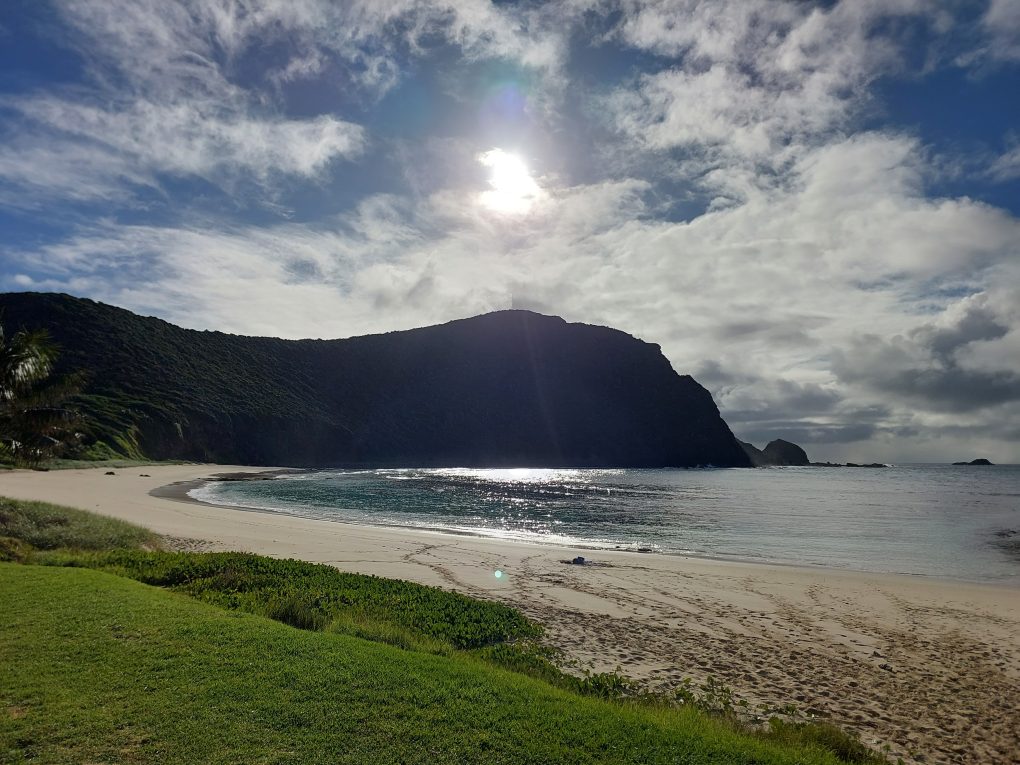 Image shows an empty beach and the sun above a cliff