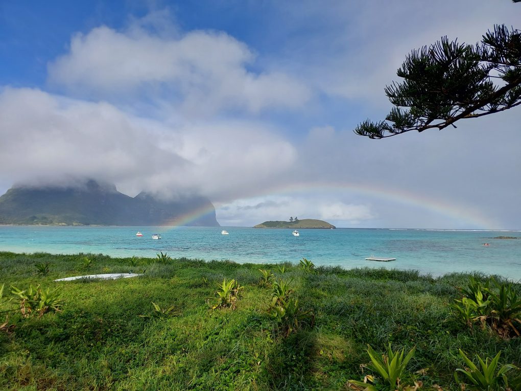 Image looking out towards Mount Gower from Lagoon Road Lord Howe Island. The mountain is hidden by clouds and there is a rainbow over the lagoon