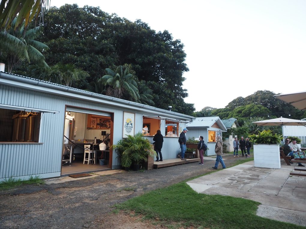 The frontage and courtyard at Lord Howe Island Brewery. Part of the Brewery interior is visible, with 2 windows where drink and food can be ordered from. 